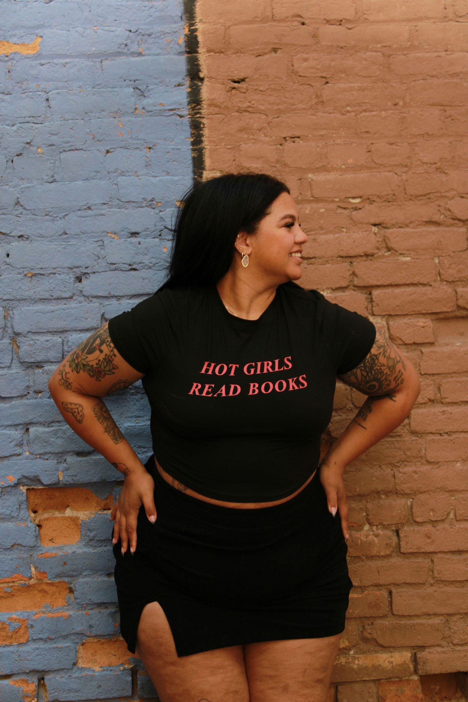 'Hot Girls Read Books' crop top styled with black skirt against painted brick wall.