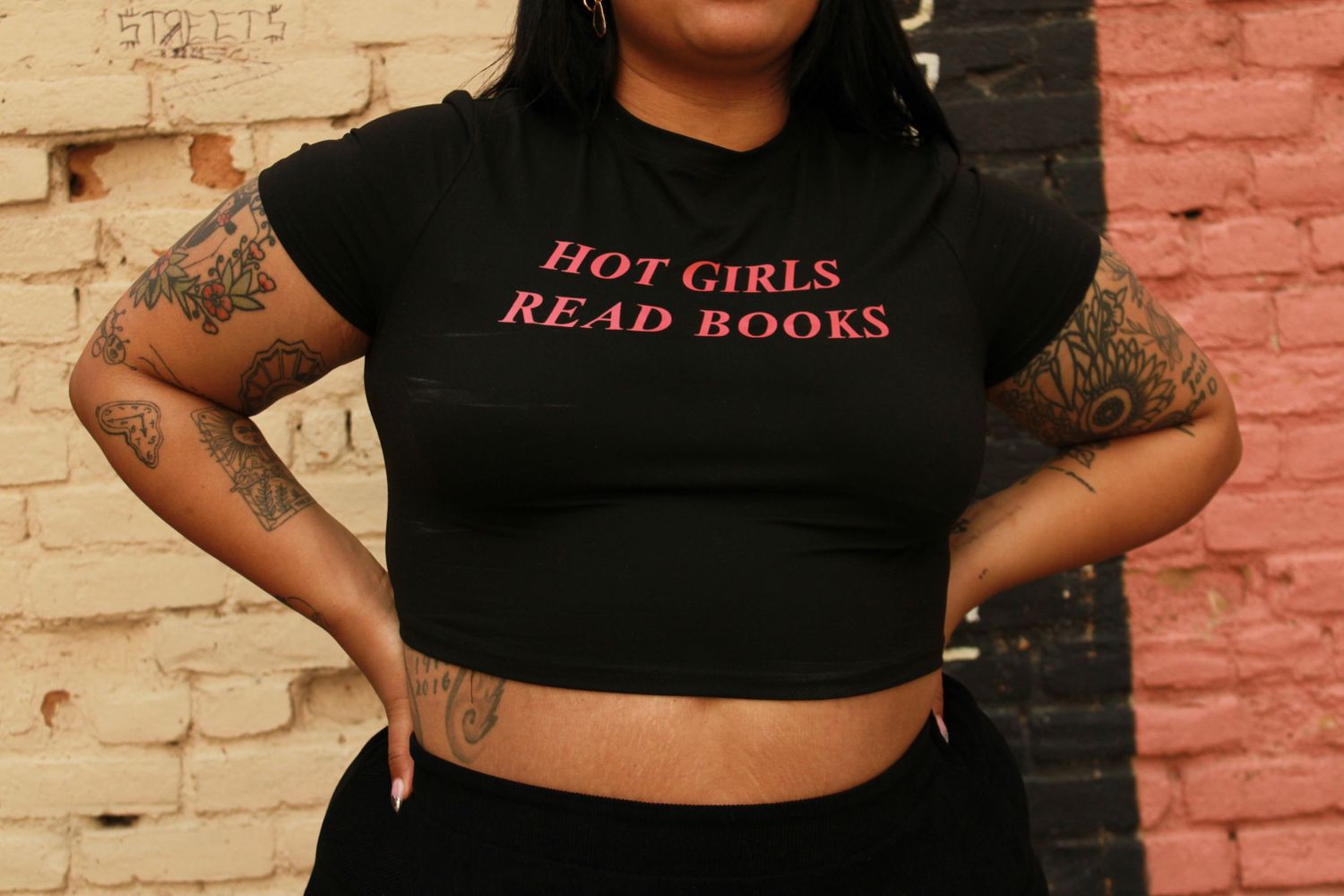 Close-up of black crop top with 'Hot Girls Read Books' text and visible arm tattoos.