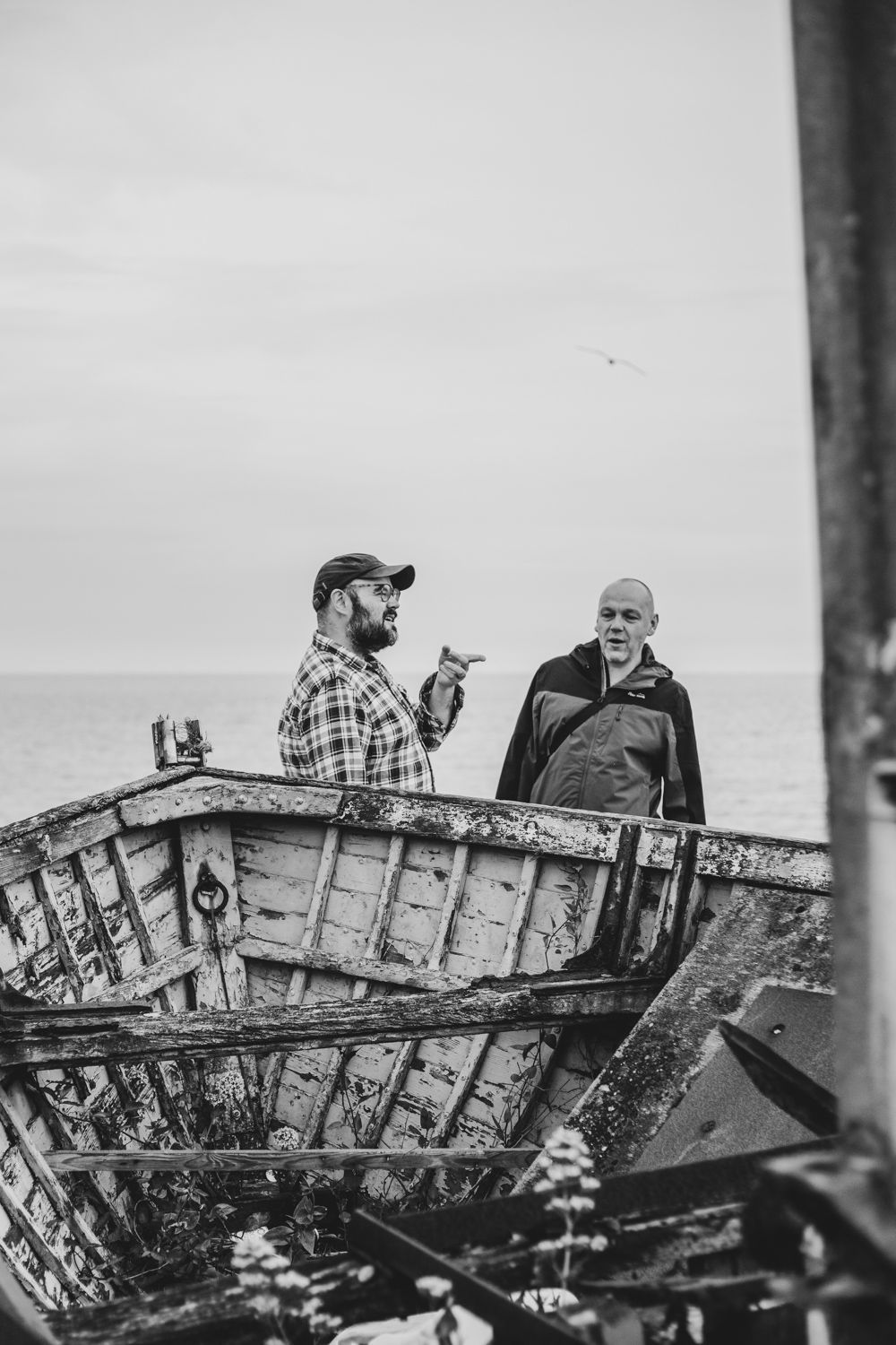 Two people having a conversation while standing in an old wooden boat by the sea. Aldeburgh Suffolk