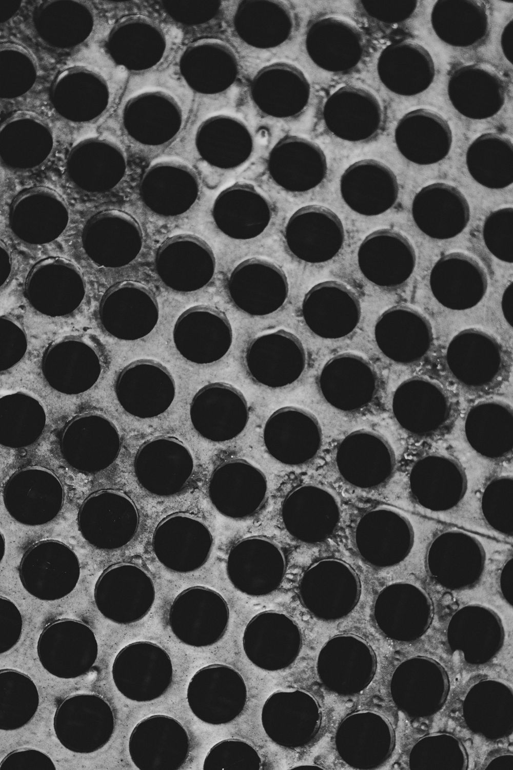 Detailed black and white photograph of a metal grate with uniform circular holes.