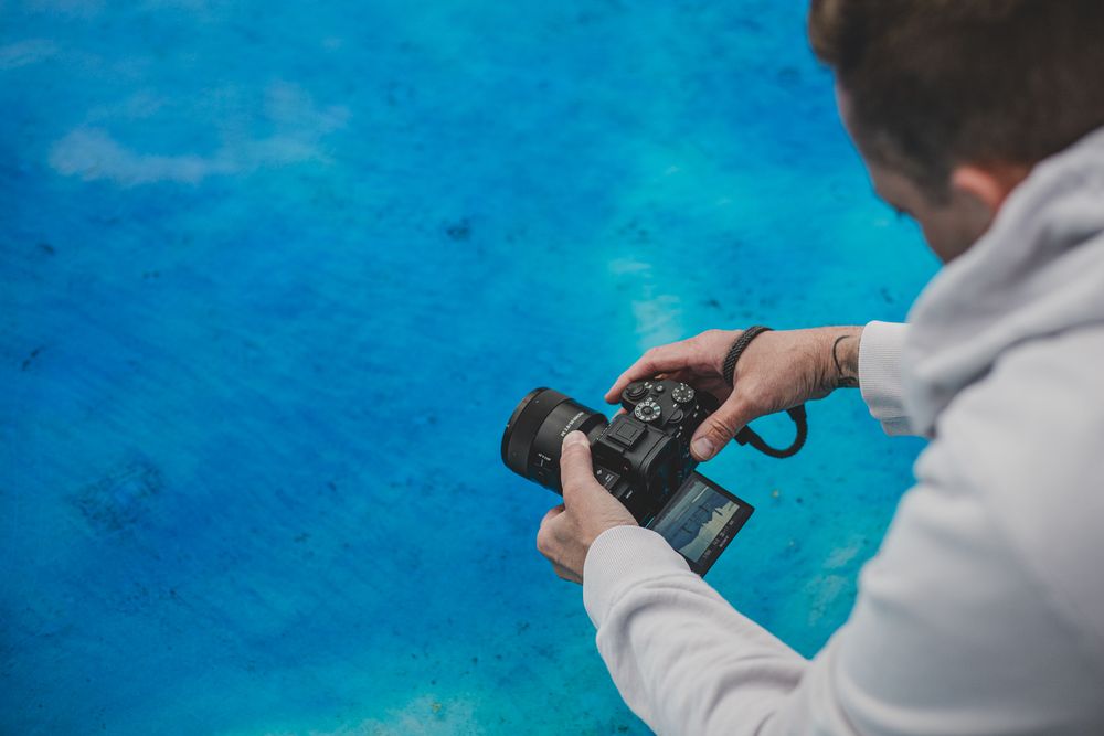 Person holding a camera pointing down at bright blue water.