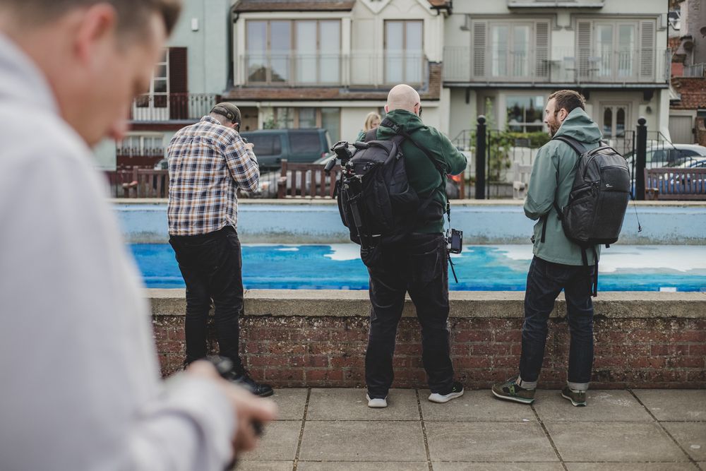 People standing at a railing overlooking a blue surface on an overcast day.