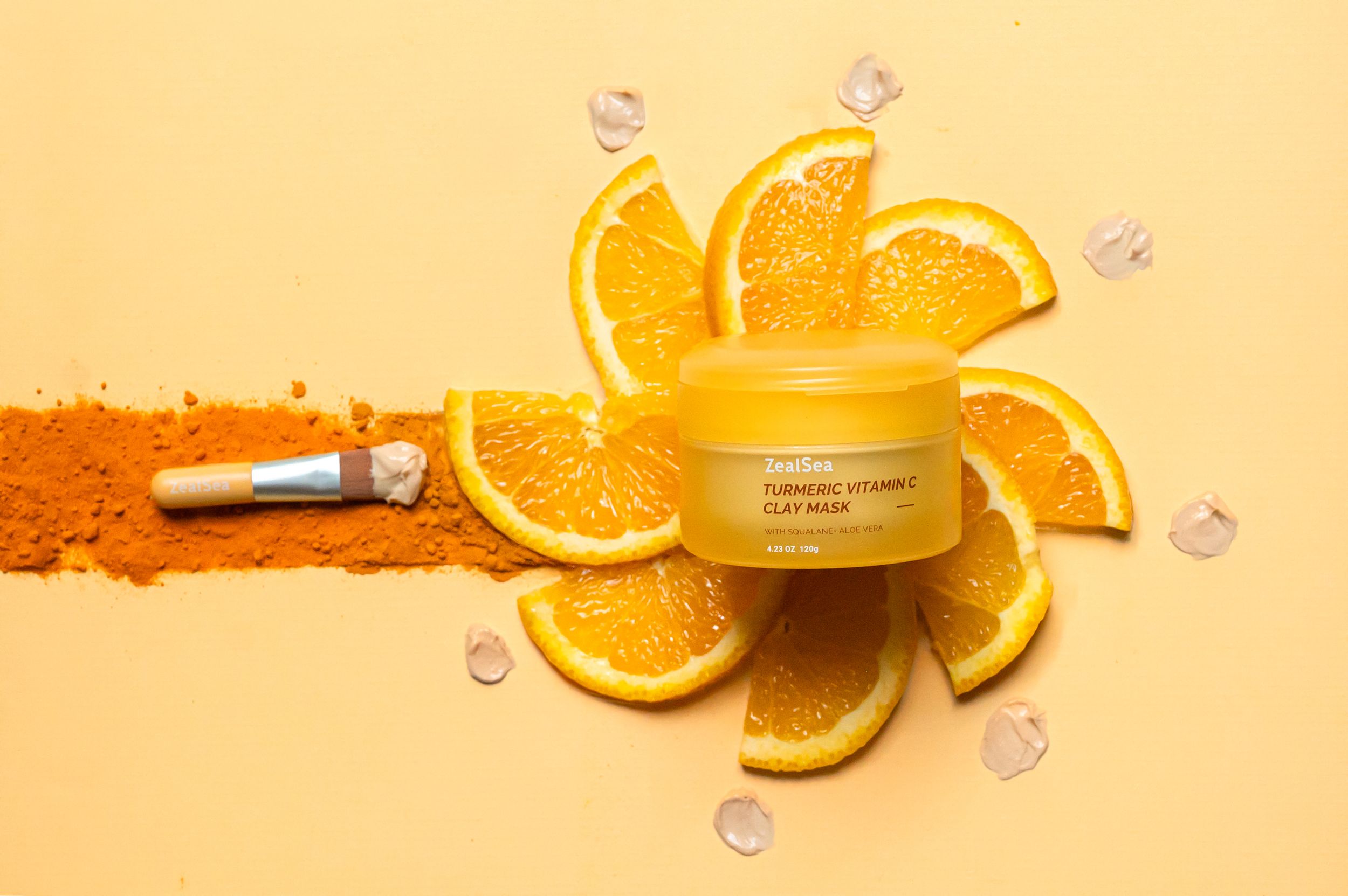 Orange-colored skincare cream jar surrounded by fresh orange slices and powder on yellow background.