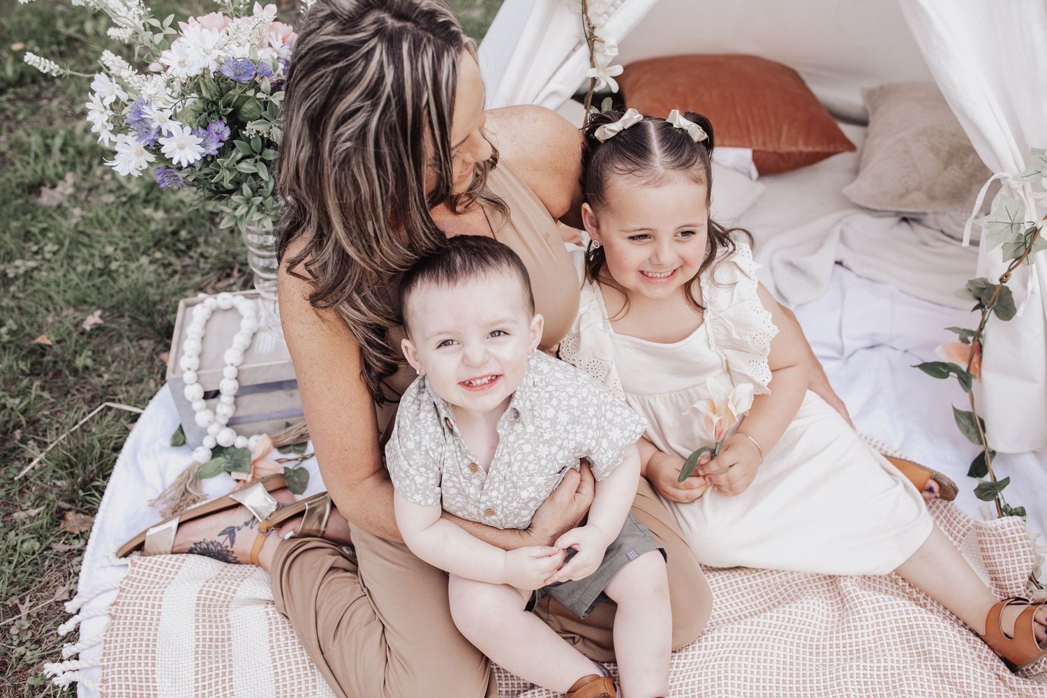 A family relaxes together on a blanket during an outdoor picnic with white decor and floral arrangements.