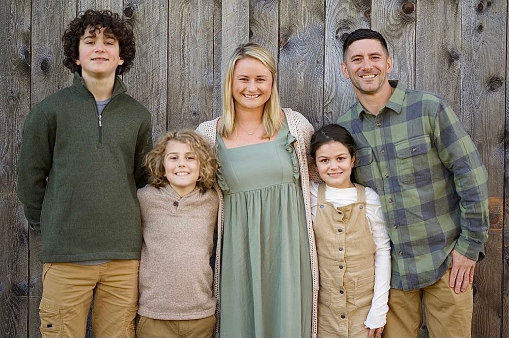 Family portrait group standing together against a rustic wooden fence background.