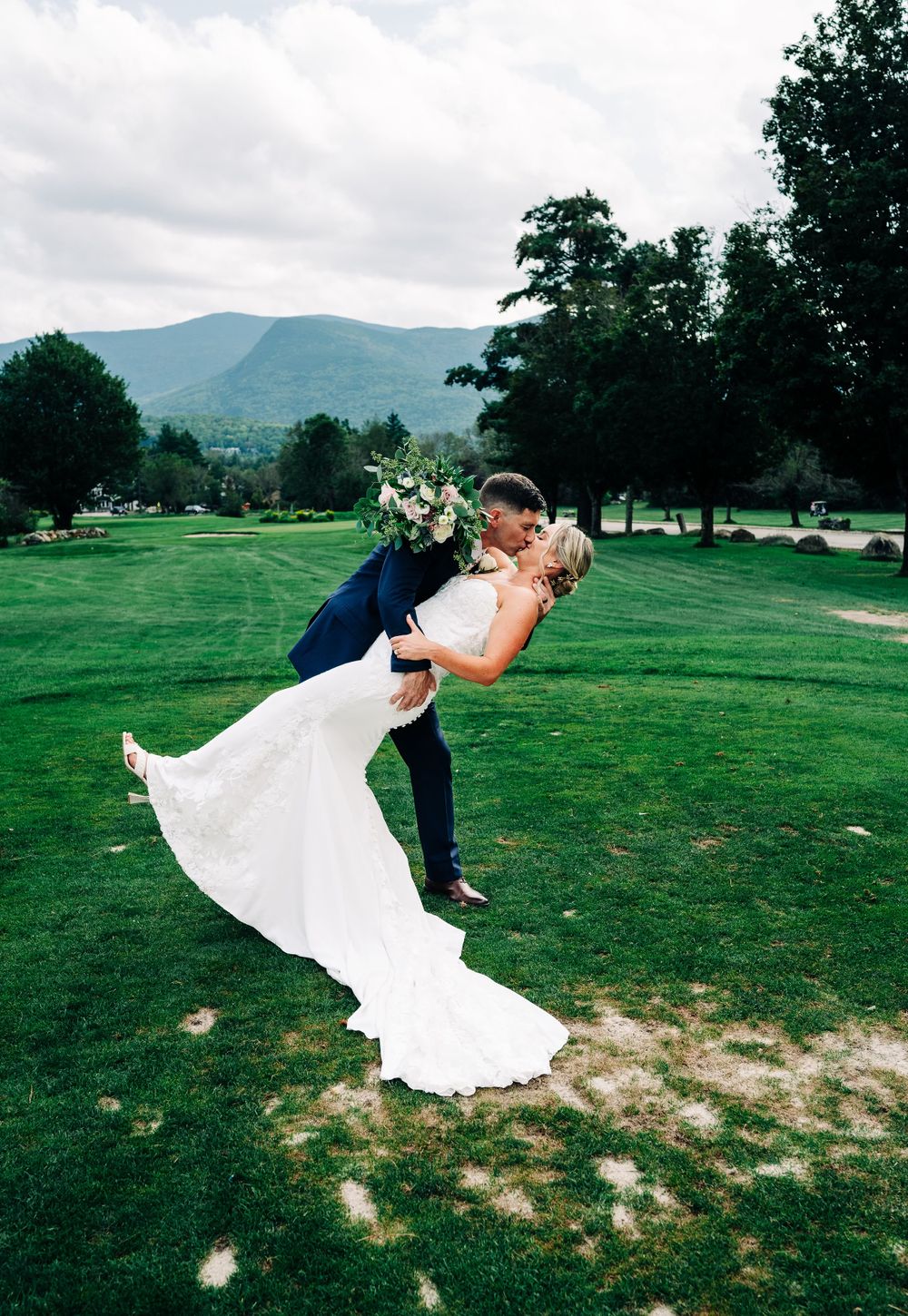 Romantic wedding couple dip kiss sequence on a green lawn with mountains in the background.