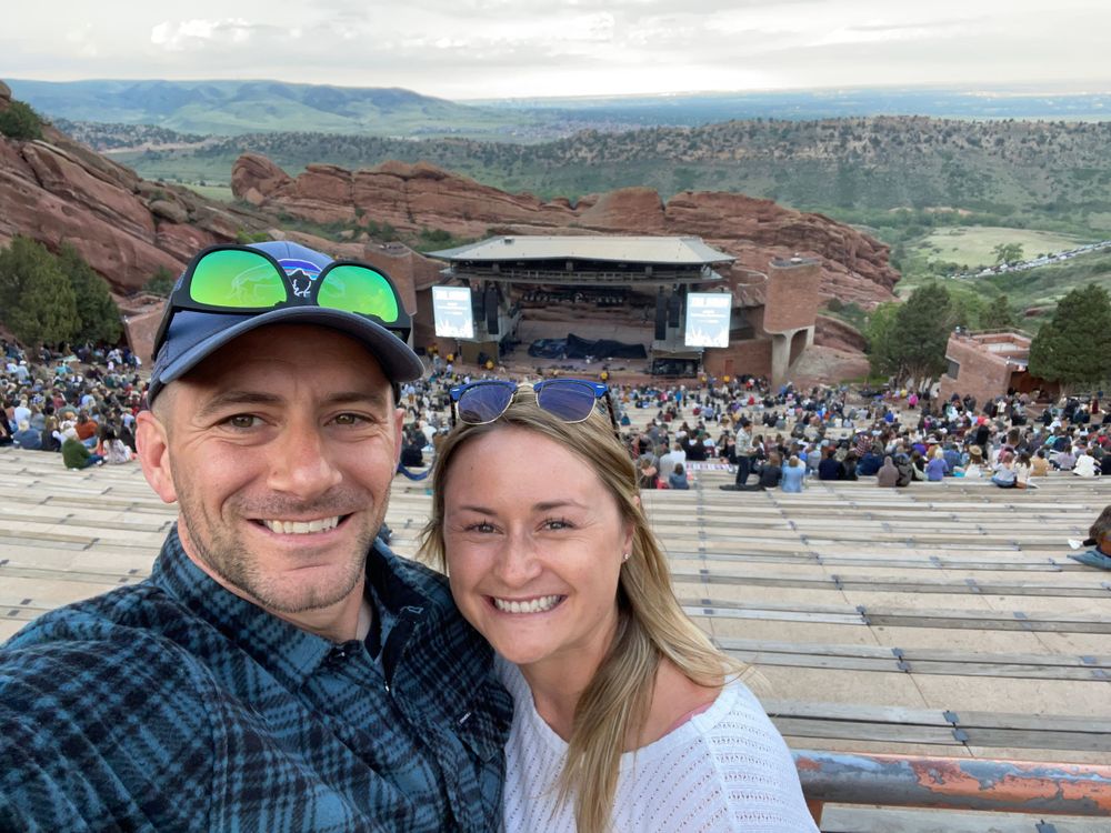Couple taking selfie at Red Rocks Amphitheatre with mountain views in background.