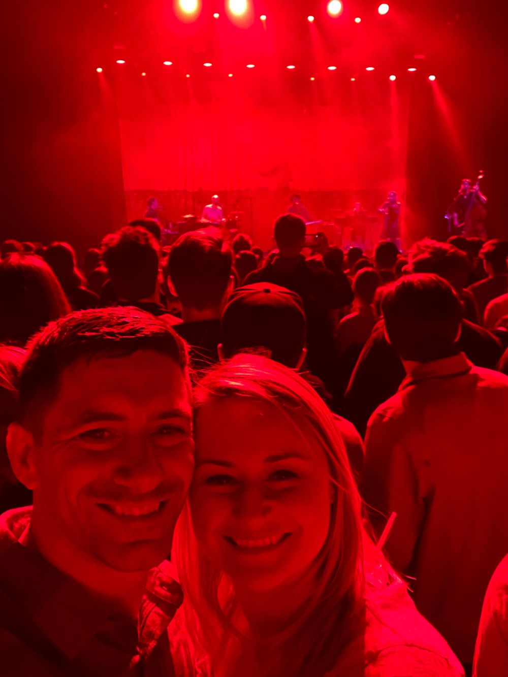 Concert crowd bathed in red lighting enjoying a live performance.