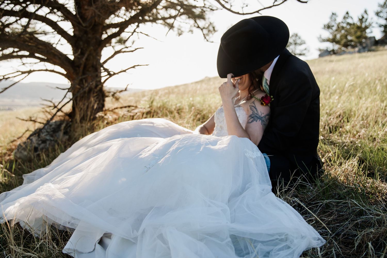 A romantic wedding photo series showing a couple embracing on a grassy hillside at sunset.