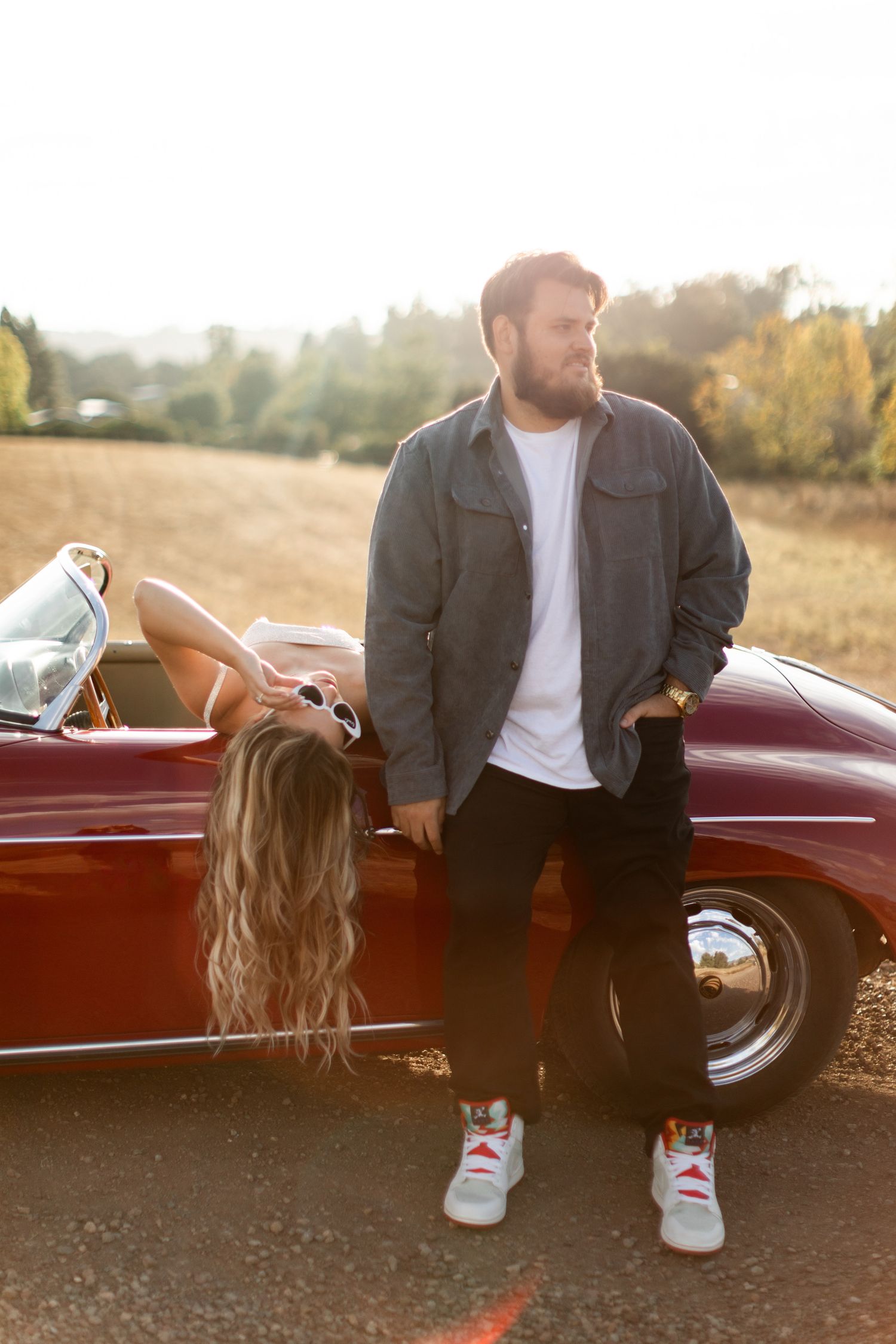 Couple sitting on vintage red car during golden hour engagement photoshoot.