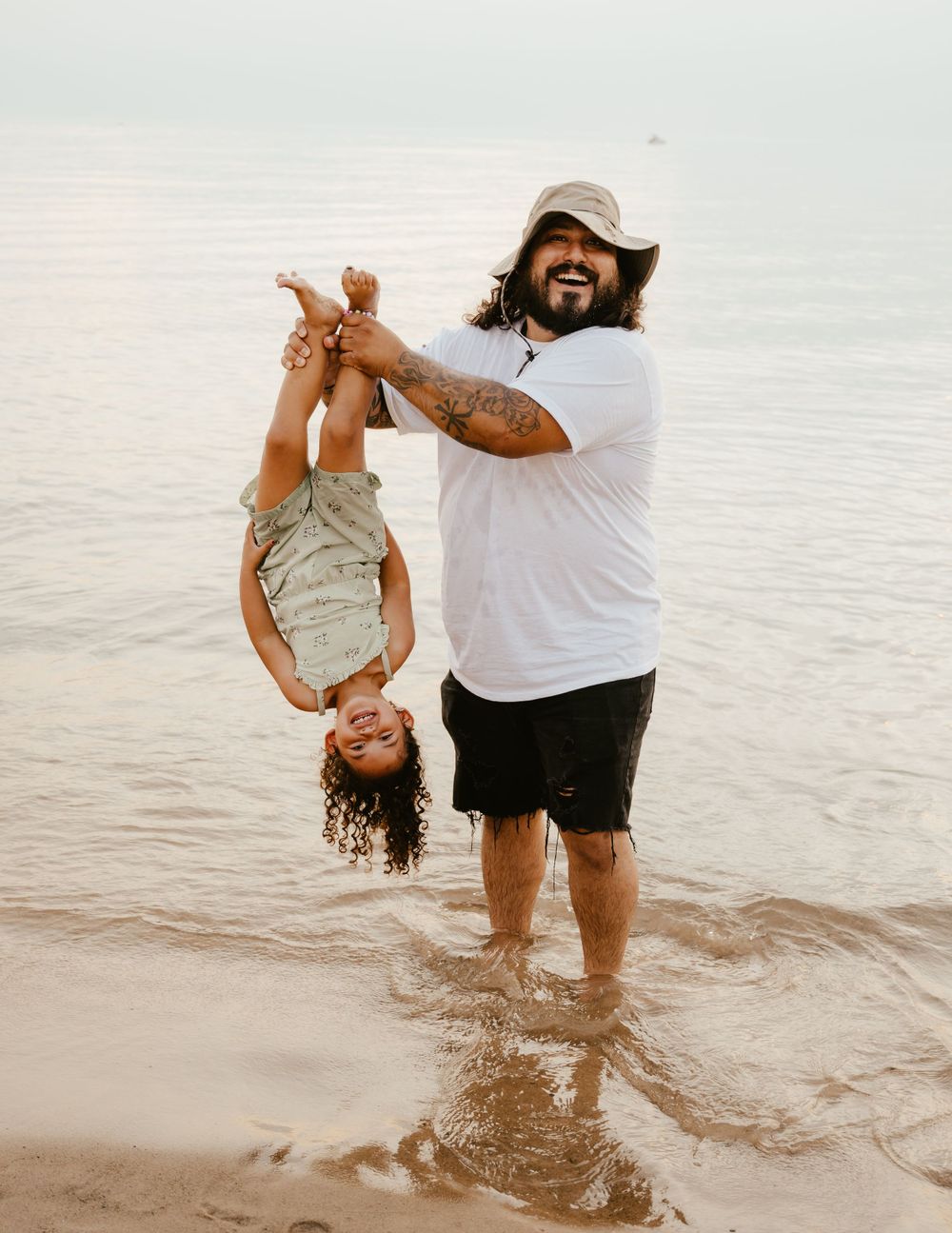 A parent and child play together in shallow ocean water during a joyful moment at the beach.