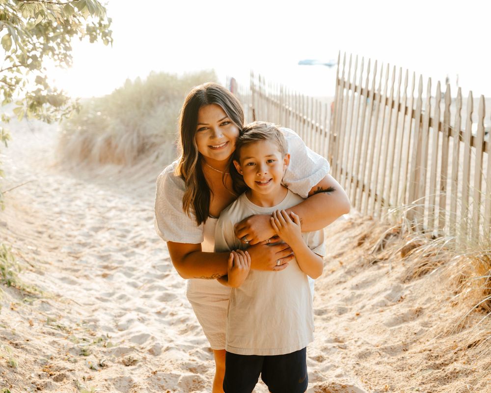 A sunny beach path with wooden fence and two people hugging and smiling together on a warm day.