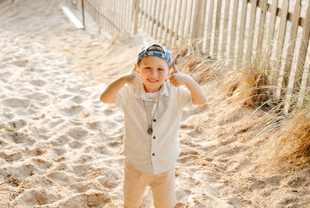 A joyful figure stands against a sandy beach path with white picket fence in golden sunlight.