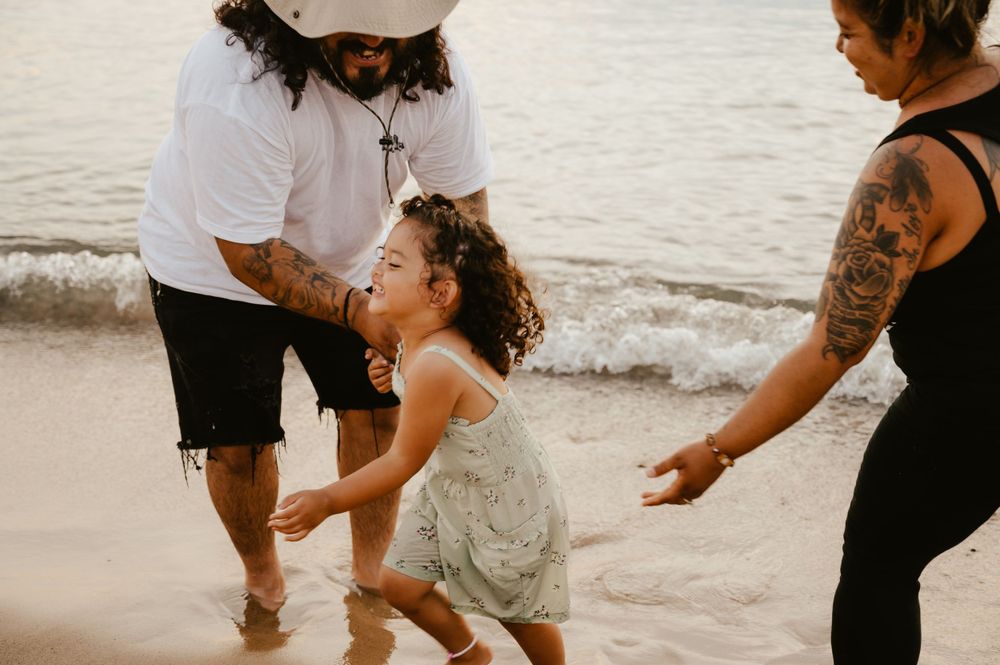 A candid family moment on a sandy beach with waves and sunset lighting in the background.