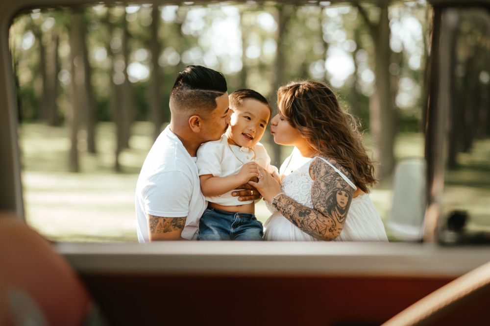 Family shares a tender moment together outdoors in a wooded setting during sunny day.