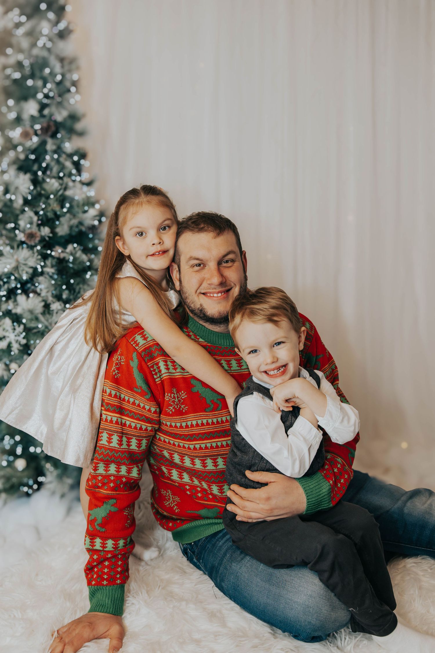 Holiday portrait in front of Christmas tree with matching festive red sweaters and white backdrop.