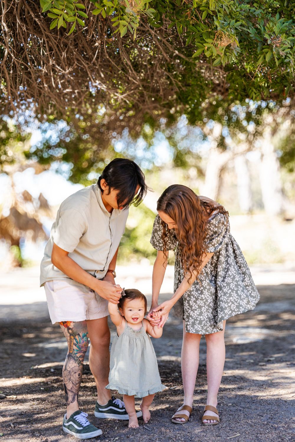 a photo of mother, father and baby holding hands under a tree