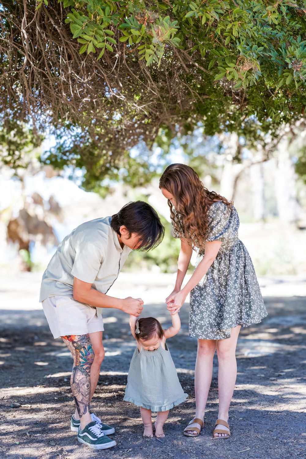 a photo of mother, father and baby holding hands under a tree