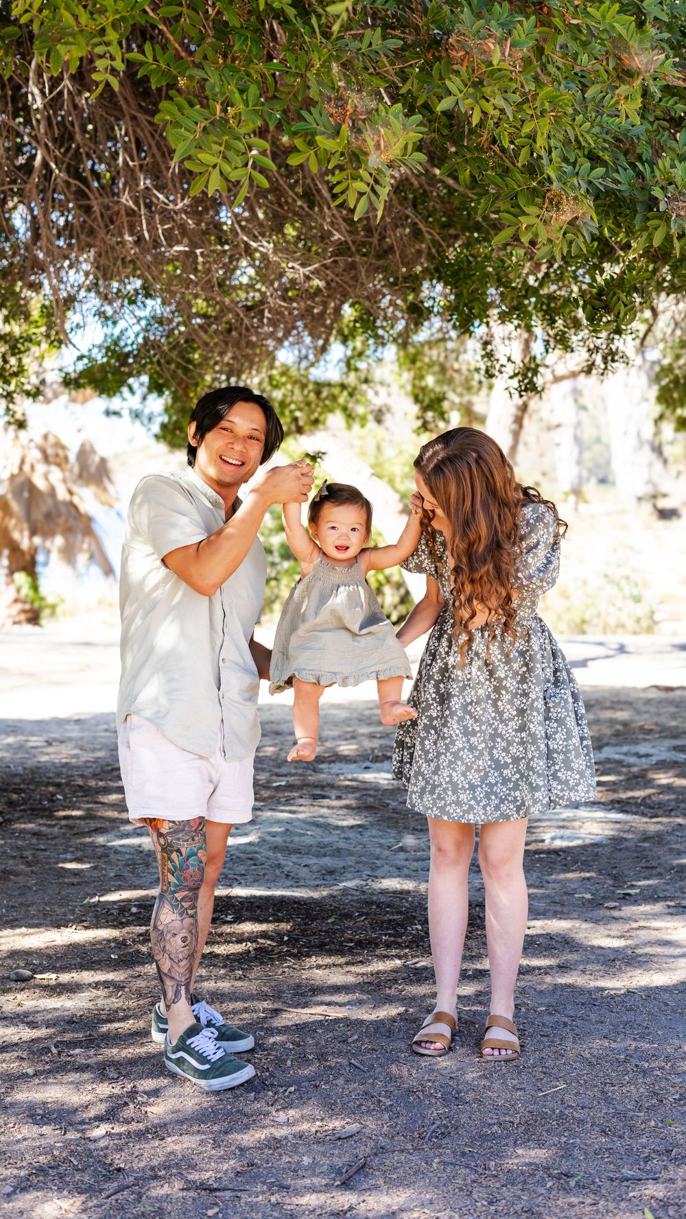 a photo of mother, father and baby playing under a tree