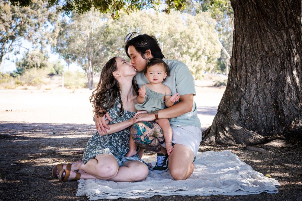 a photo of mother, father and baby sitting under a tree