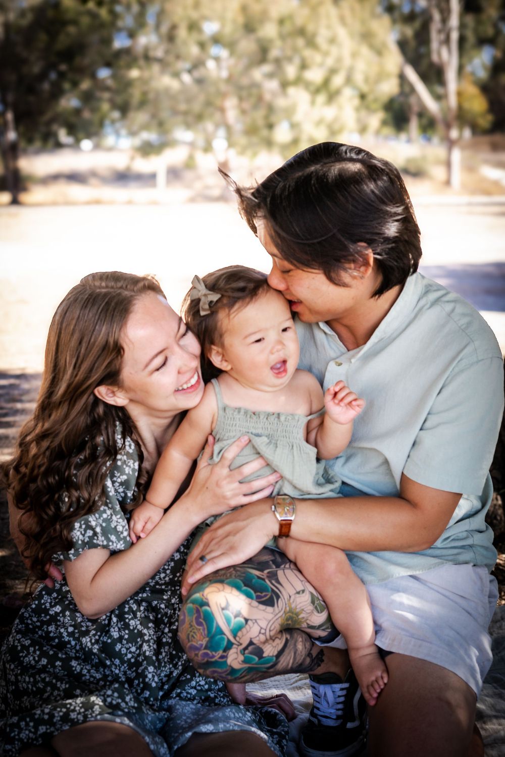 a photo of mother, father and baby under a tree