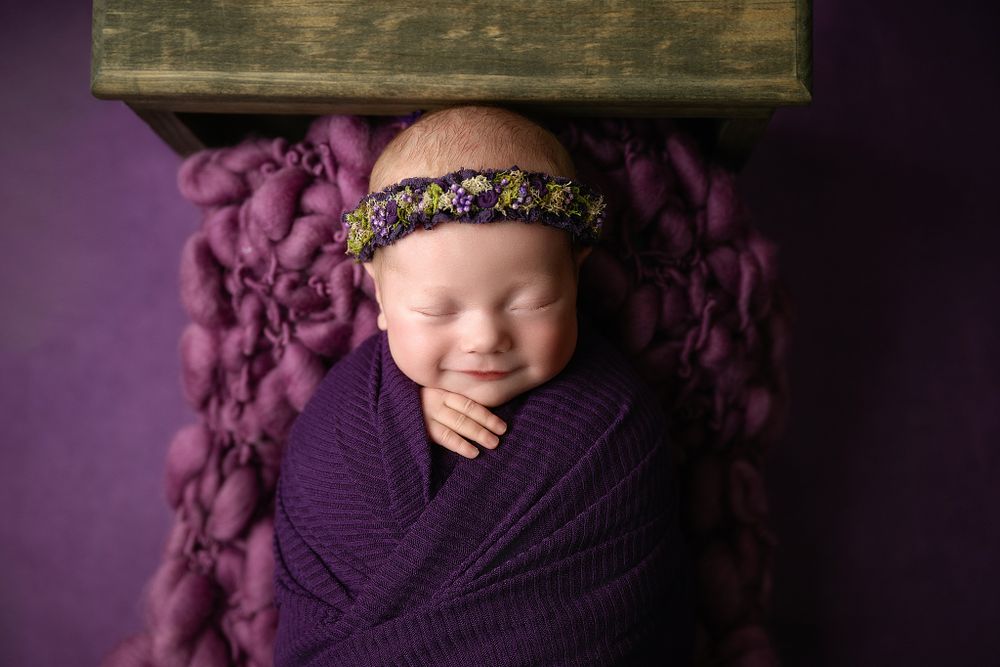 Peaceful sleeping newborn wrapped in purple knit with delicate headband.