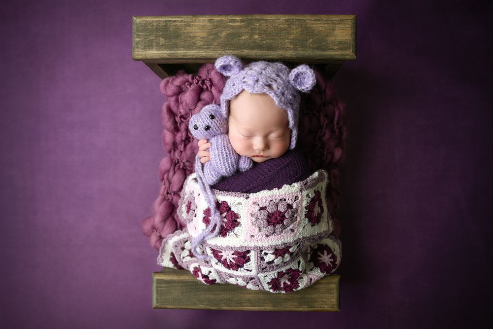 Sweet newborn photo with bear bonnet and floral wrap in wooden box.