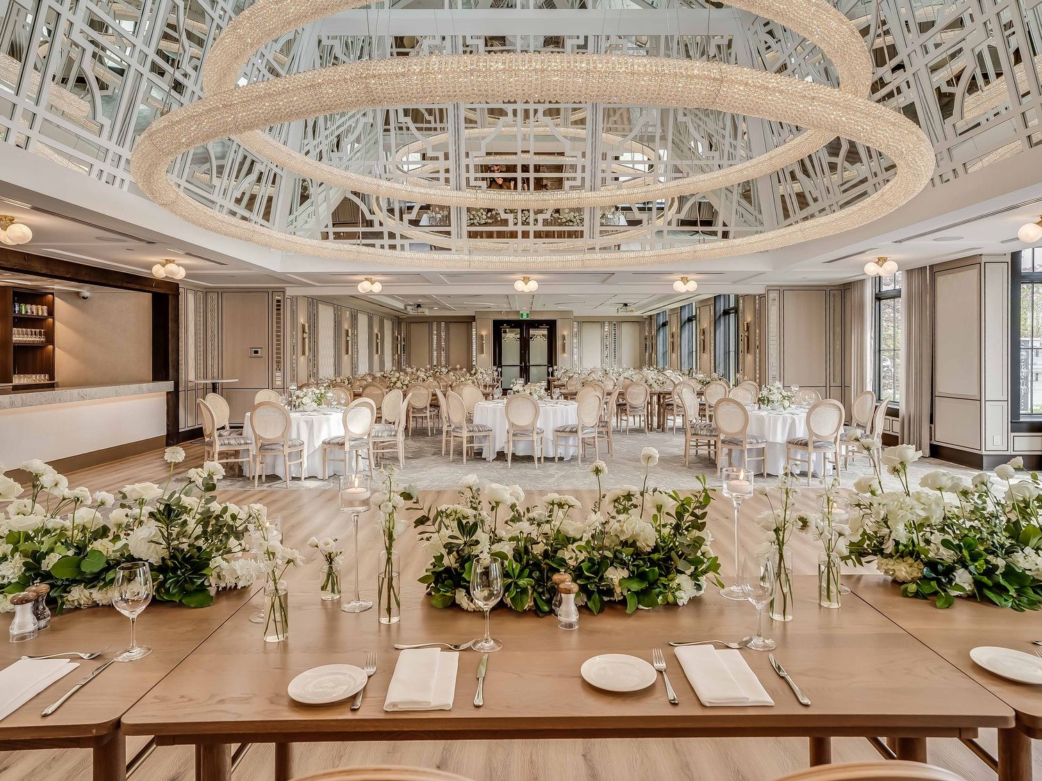 Luxurious white wedding reception hall with ornate ceiling details and floral centerpieces.