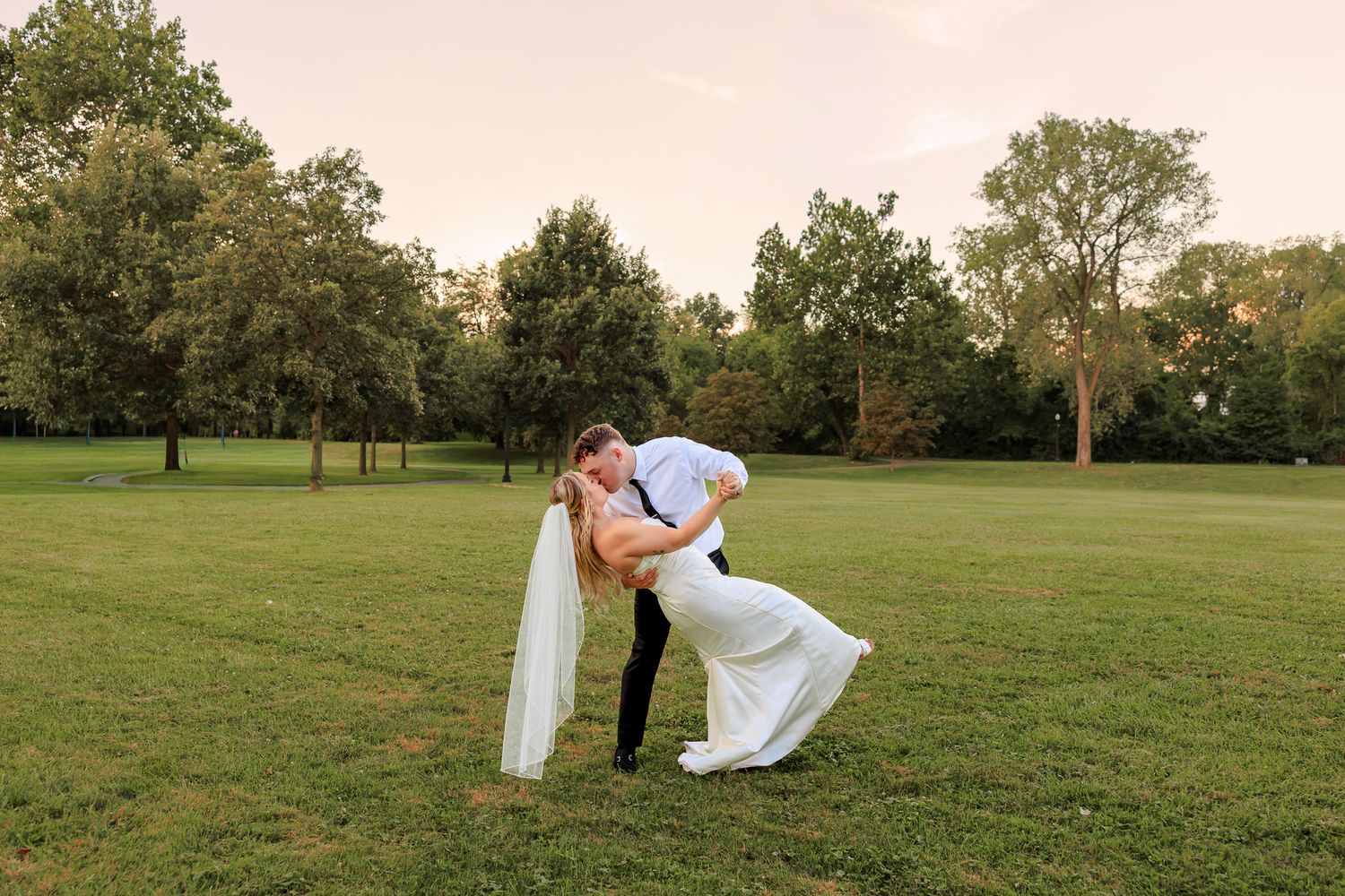 Wedding party in emerald and black attire poses on grassy hill during autumn ceremony.
