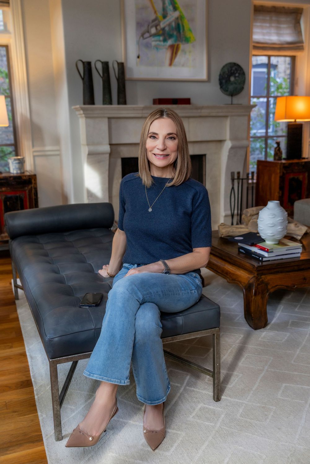 Person wearing navy top and blue jeans sits casually in a modern gray armchair on a patterned area rug.