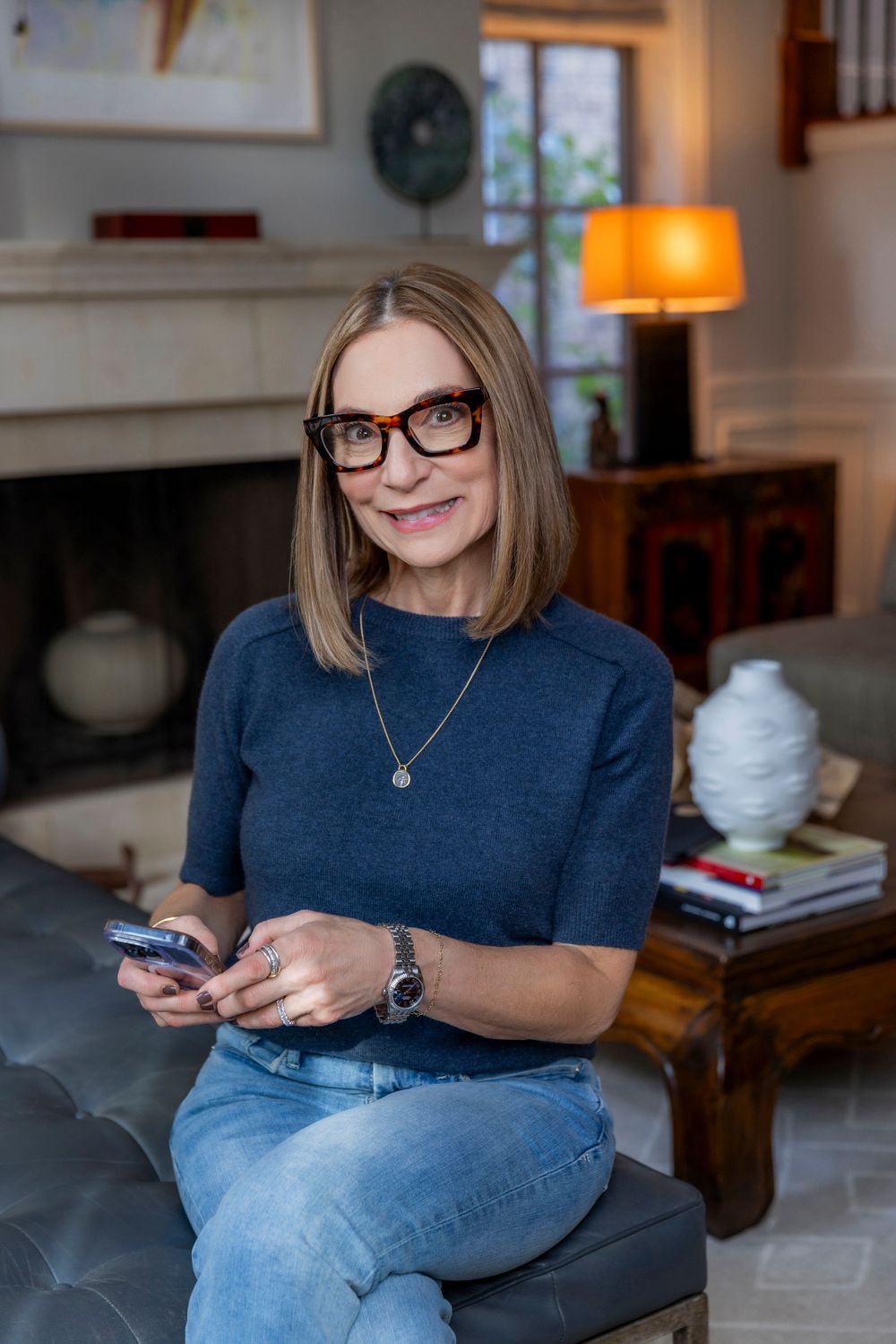 Person in blue shirt and jeans sits casually while texting or using smartphone in home setting.