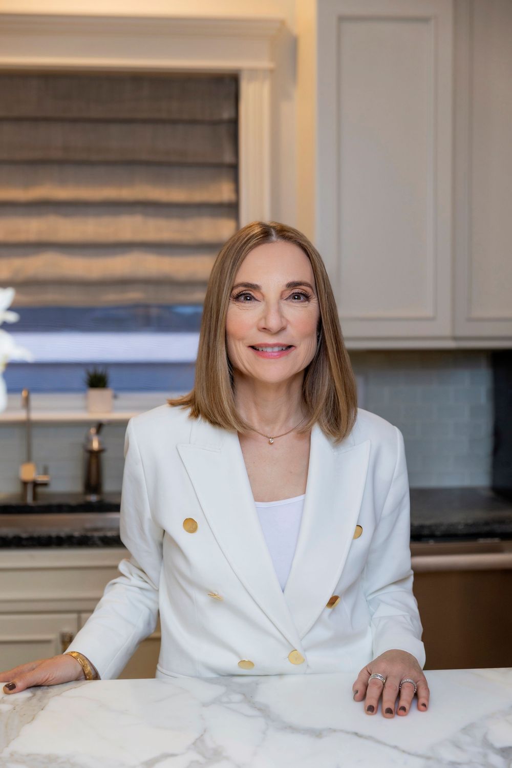 Professional headshots of someone wearing a crisp white blazer with gold buttons in a modern kitchen setting.