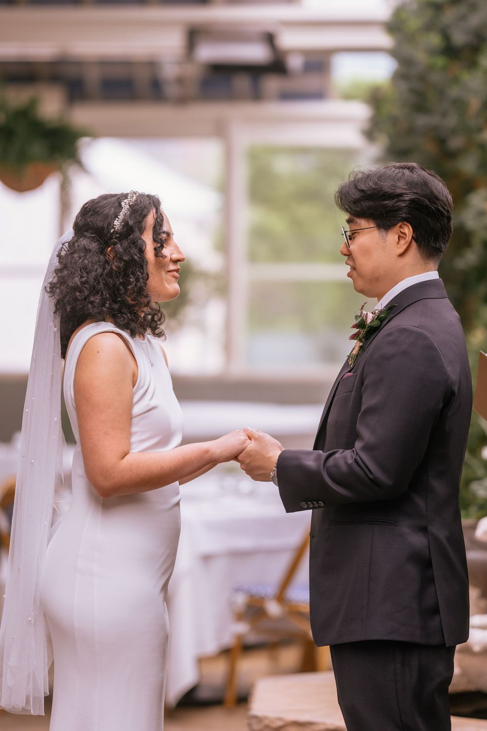A bride and groom hold hands and exchange vows during their wedding ceremony in an elegant indoor venue.