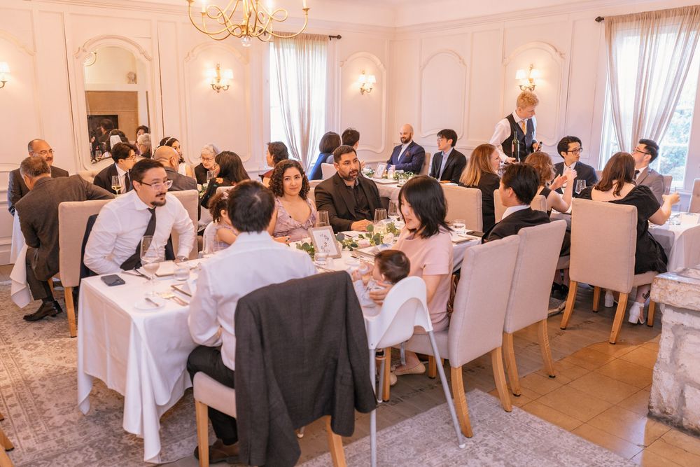 Elegant wedding reception dinner with guests seated at decorated tables in a bright, upscale venue.