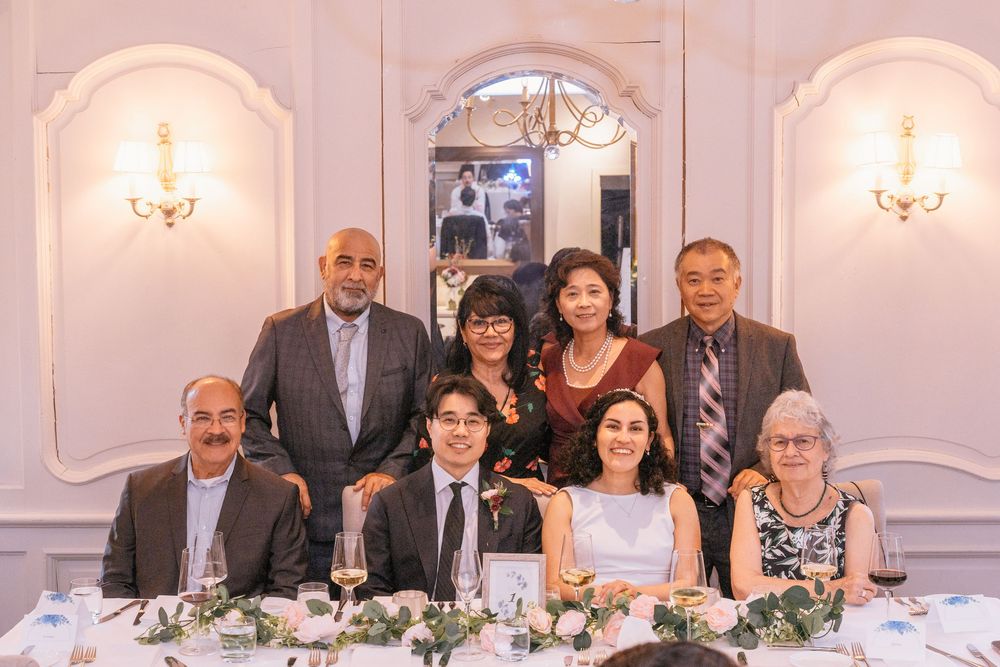 Group of eight people posing together at an elegant wedding reception dinner table with floral centerpieces.