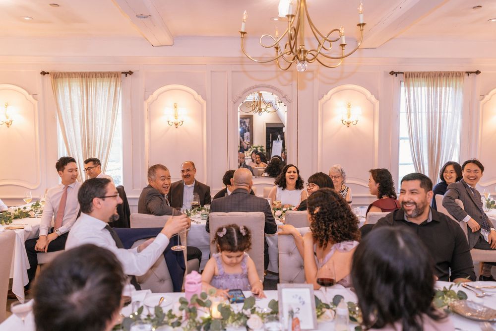 Elegant wedding reception with guests seated at decorated tables in a bright, ornate banquet hall with chandeliers.