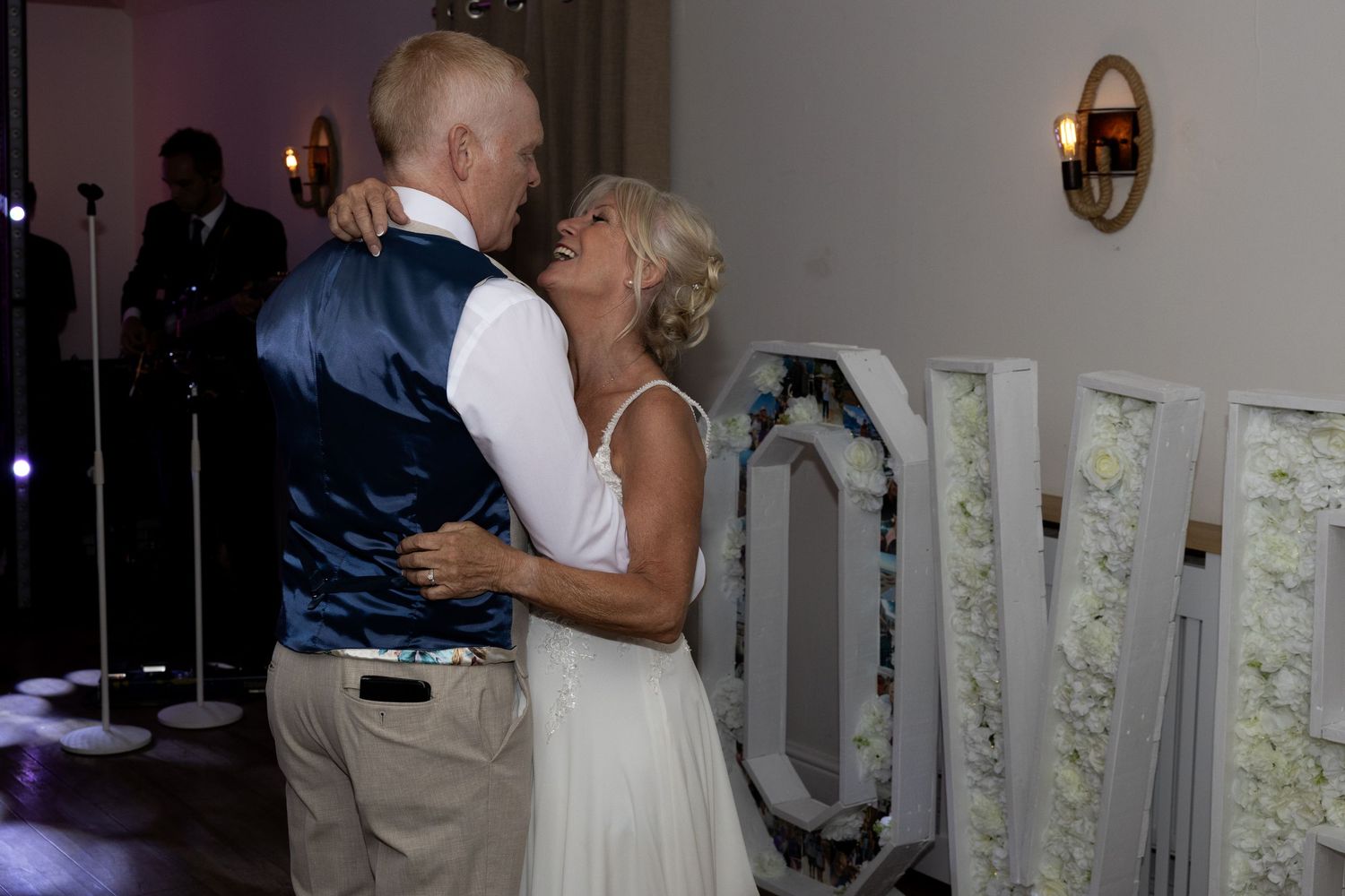 Bride and groom exchanging rings during outdoor wedding ceremony, guests seated in background.