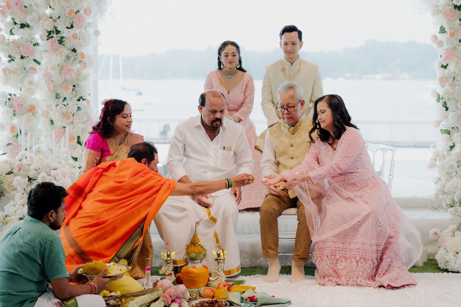 Indian family performing traditional wedding rituals outdoors, adorned in colorful ethnic attire with floral decorations.