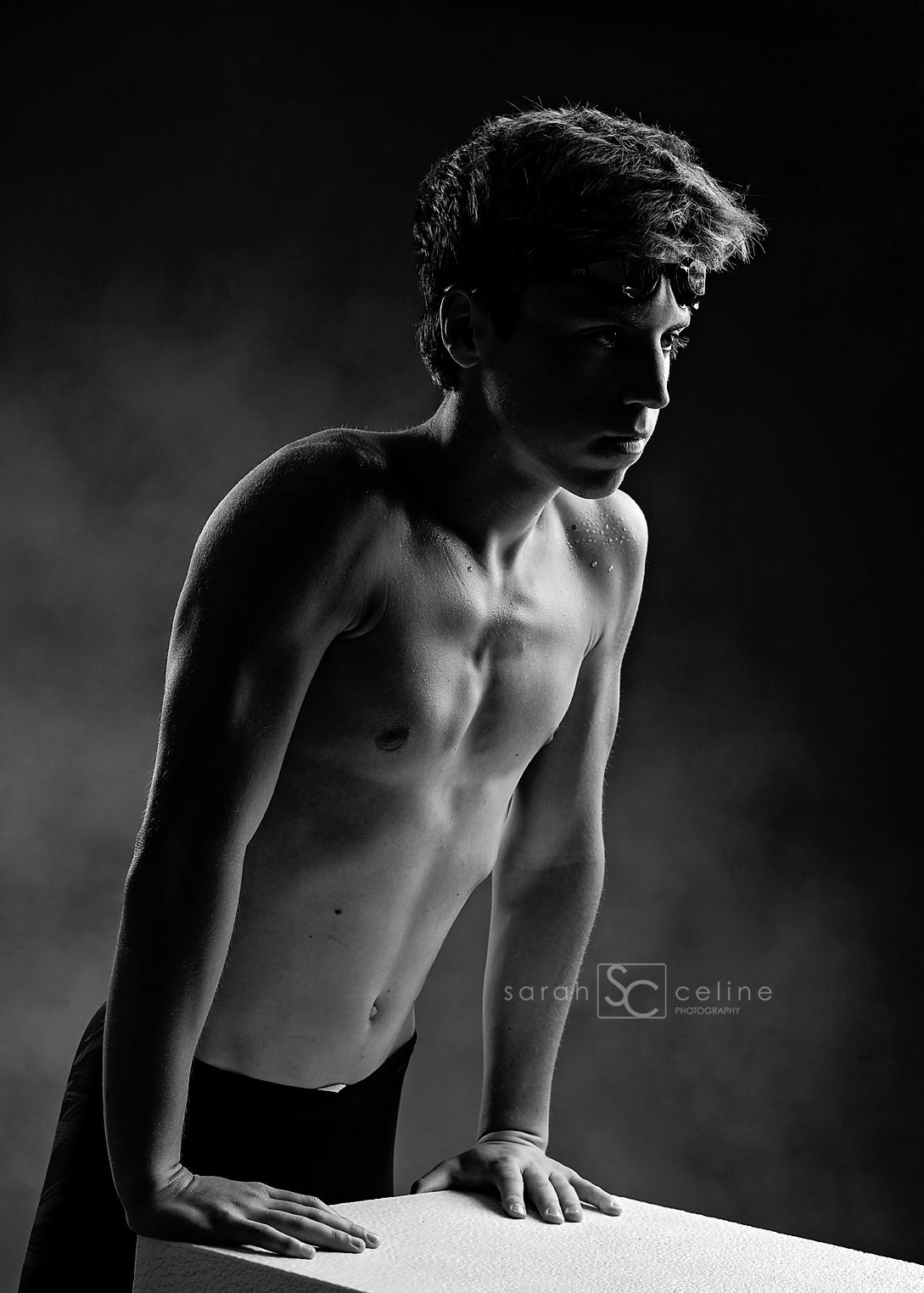 Black and white portrait of a shirtless young male athlete posing dramatically against a dark smoky background.