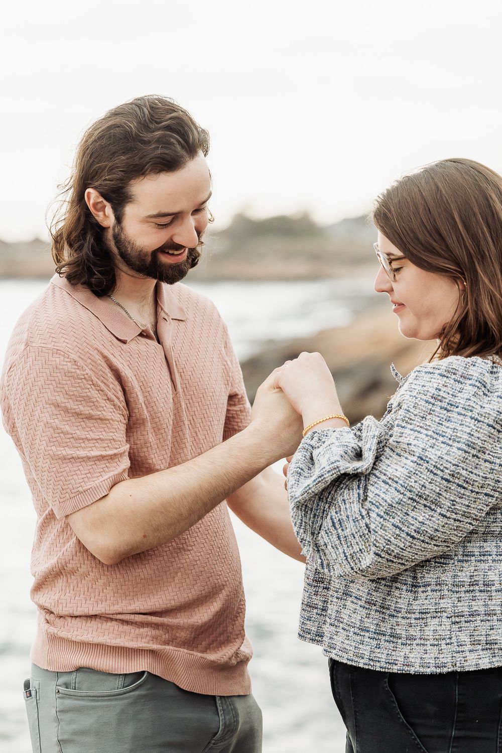 Happy bearded man placing ring on womans finger by the ocean.