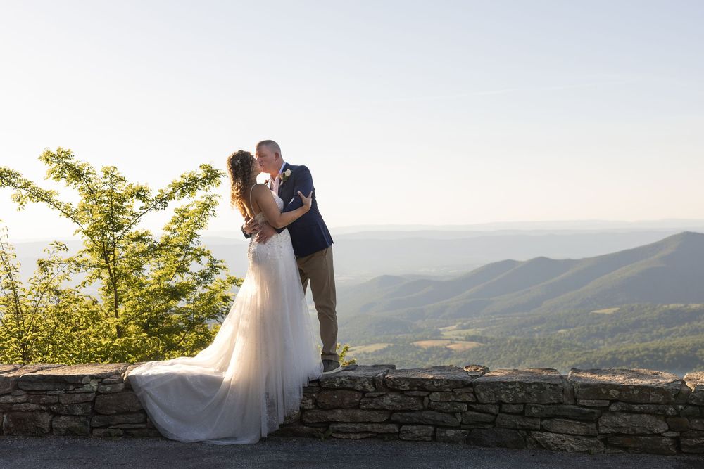 Bride and groom share a kiss at a scenic mountain overlook with sweeping green valley views on their wedding day.
