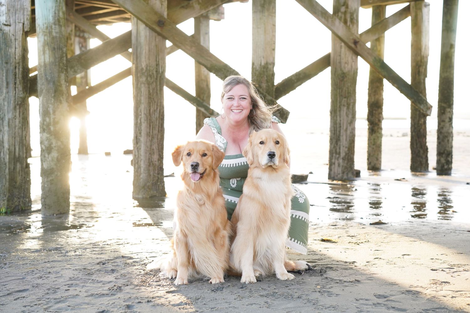 A couple smiles with their golden retriever wearing a festive Christmas bandana for a holiday portrait.
