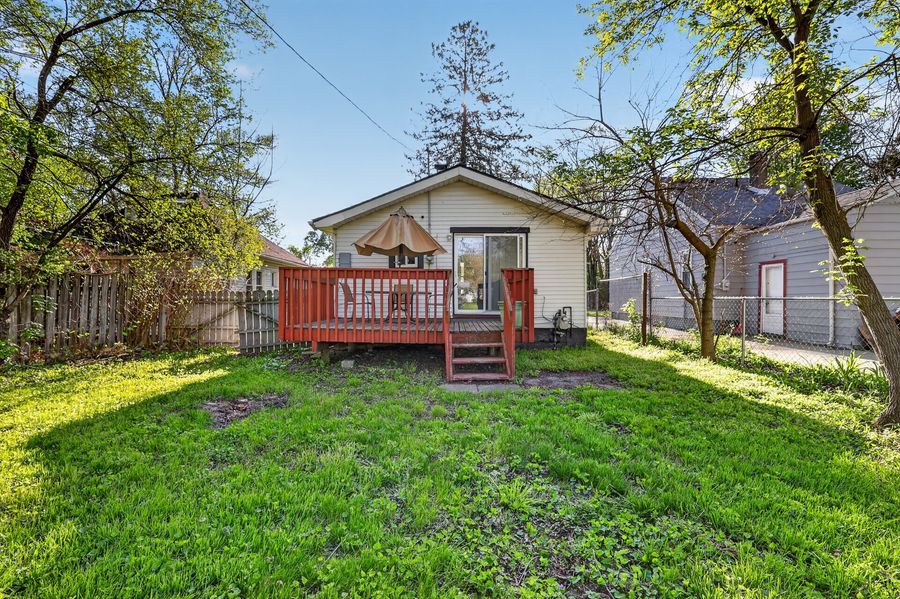 Charming cottage home with red wood deck, lush green yard, and mature trees in spring.
