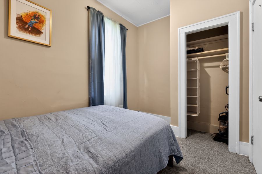 Cozy bedroom with gray bedding, beige walls, a framed artwork, blue curtains, and an open walk-in closet.