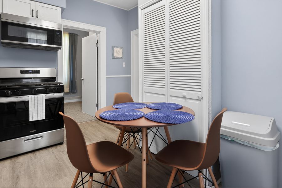 Small dining area with round blue table, brown chairs, near a stainless steel stove and white louvered closet doors.