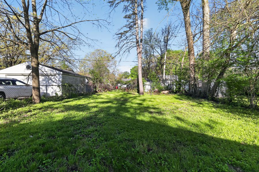 Spacious green backyard with tall trees, lush grass, and a white garage visible on the left side of the property.