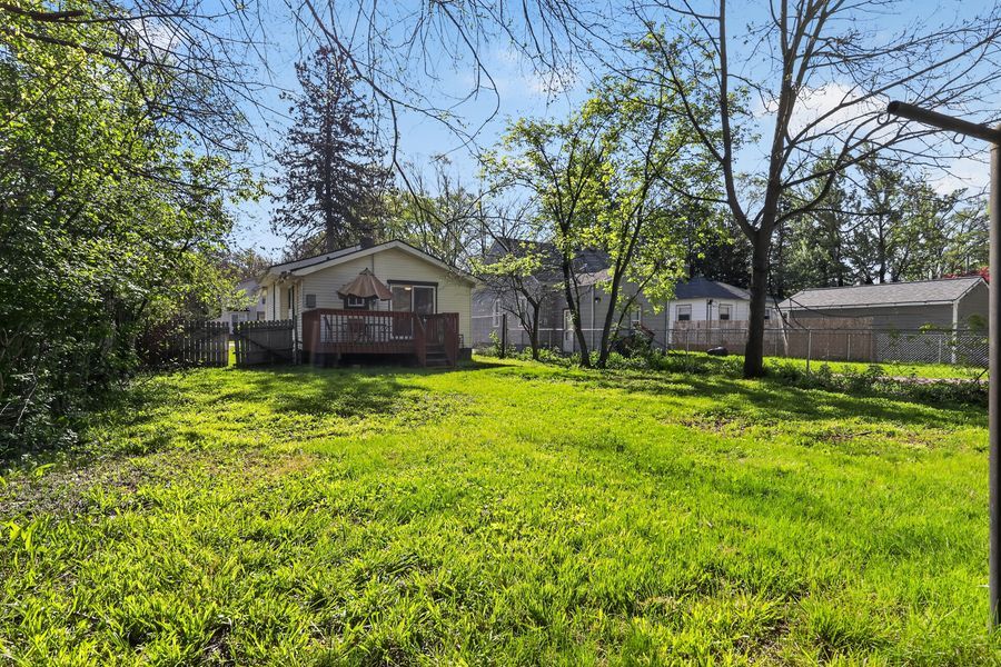 Spacious backyard with lush green lawn, mature trees, wooden deck, and white storage shed in a residential setting.
