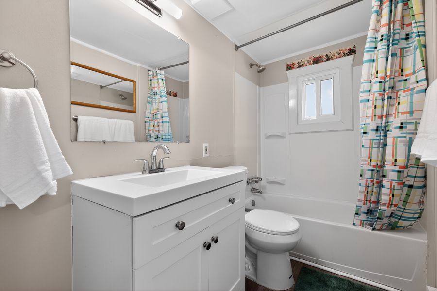 Clean bathroom with white vanity, large mirror, toilet, and a shower-tub combo with colorful curtain.