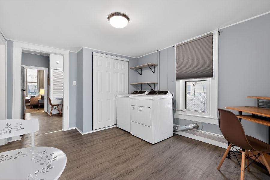 Laundry room with white washer and dryer, wood floors, closet, and shelving in a cozy home.