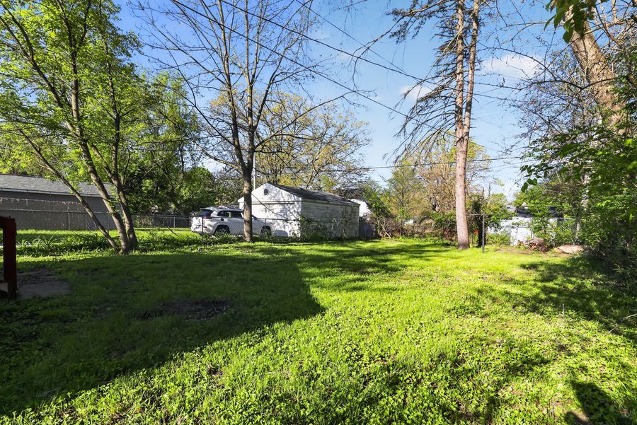 Spacious backyard with lush green grass and mature trees surrounding a residential property.